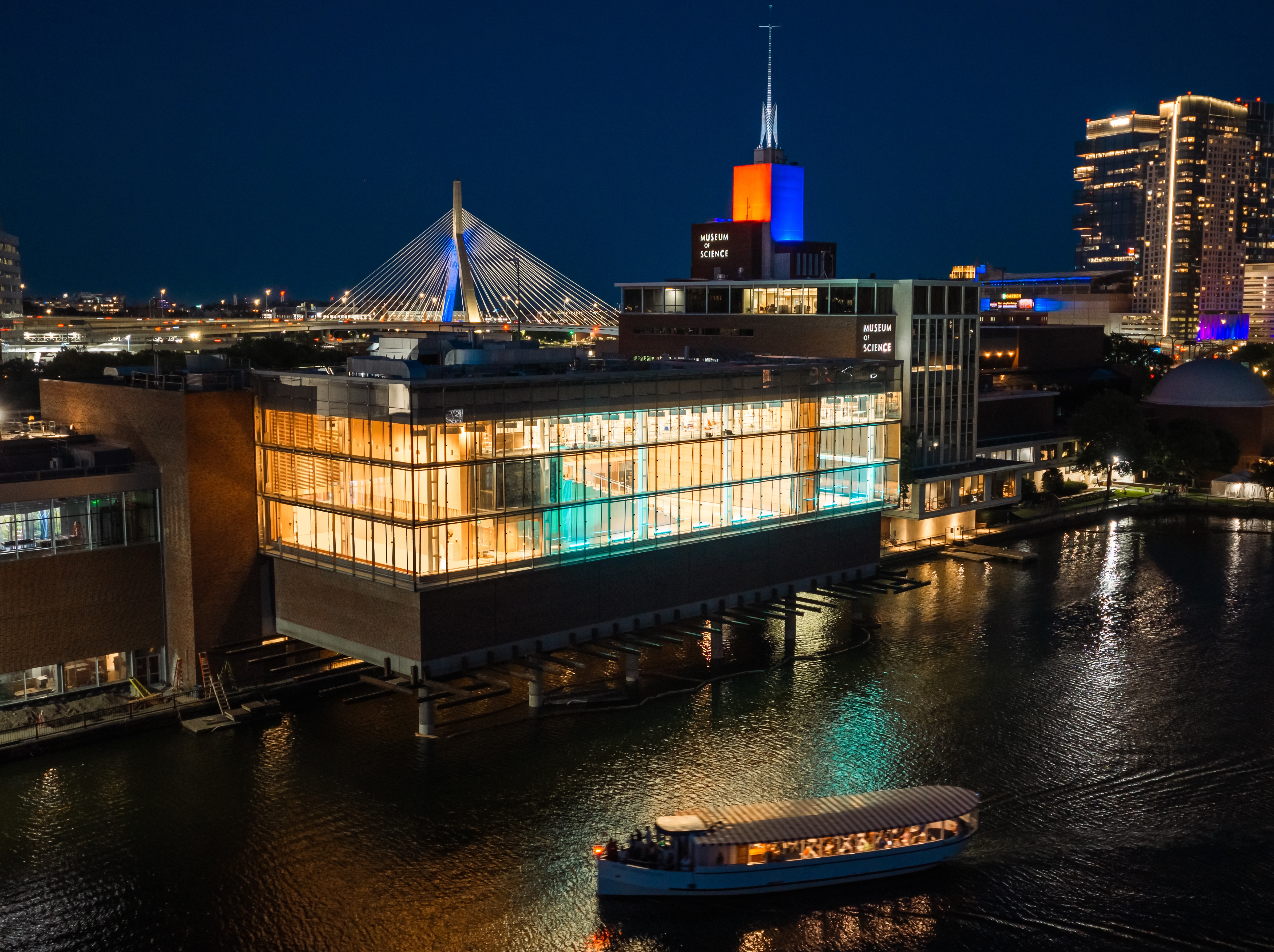 The Museum of Science and its illuminated waterfront venue at night, with the Boston skyline behind it.